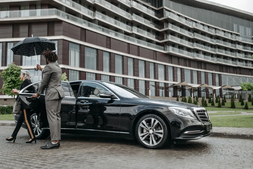 Driver with an umbrella meeting a passenger at a black sedan